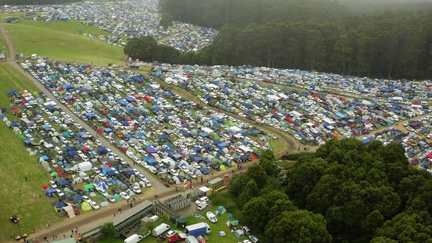 People walk along dirt road near large grassy parking lots near forest
