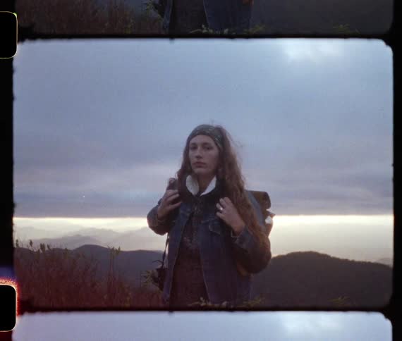 Woman with a backpack standing in front of the mountains on an overcast day