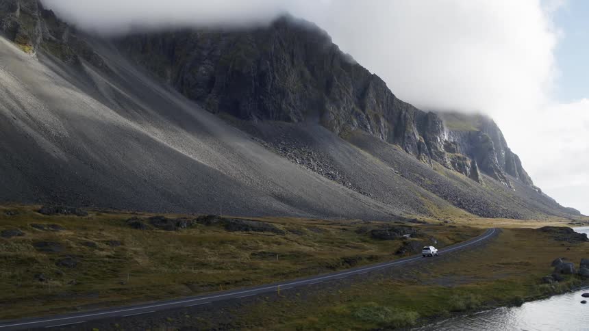 A car drives along the shore by the mountain