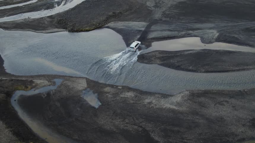 An suv travels off road through a stream in a barren area of a grassland