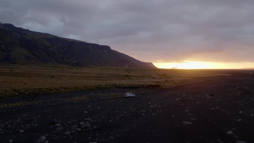 An suv traveling offroad through a rocky countryside near a mountain on a cloudy day