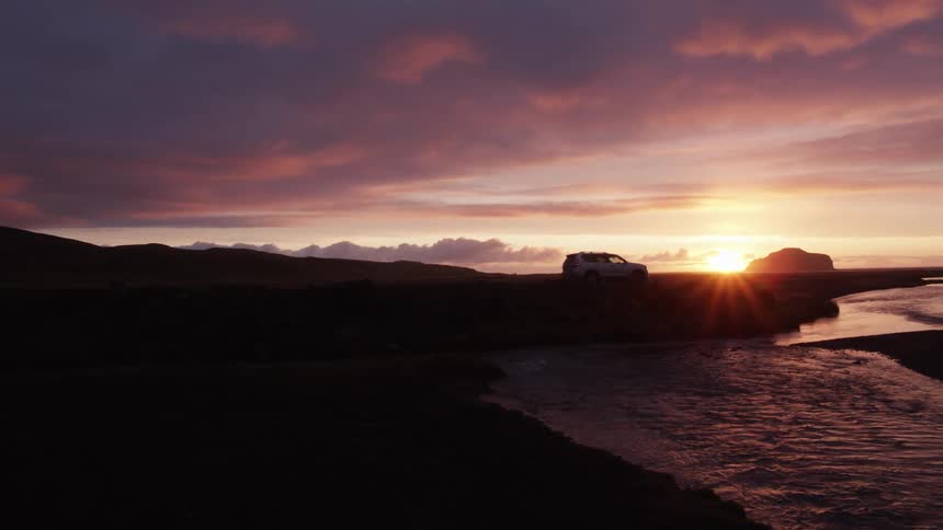 Car parks near riverbank as sun hovers on horizon turning sky red