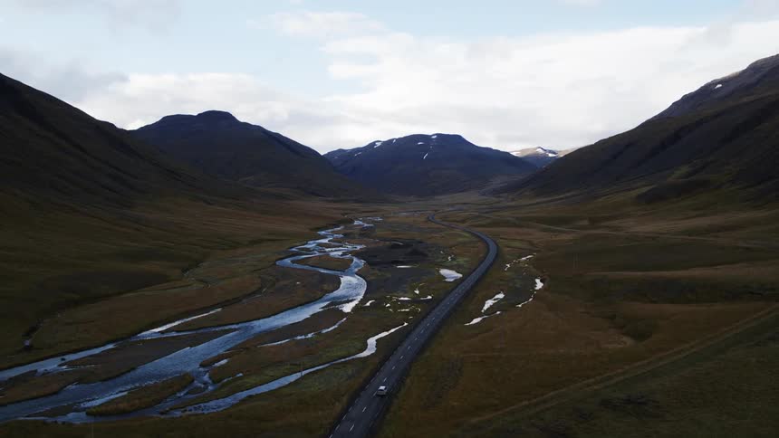 A car travels on a rural road winding through a valley next to streams of water