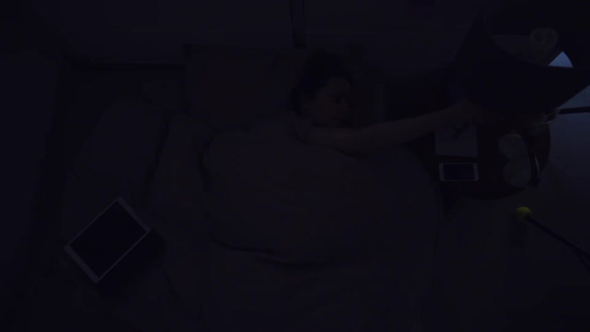 A woman reaches out from under the covers to turn off her bed side lamp