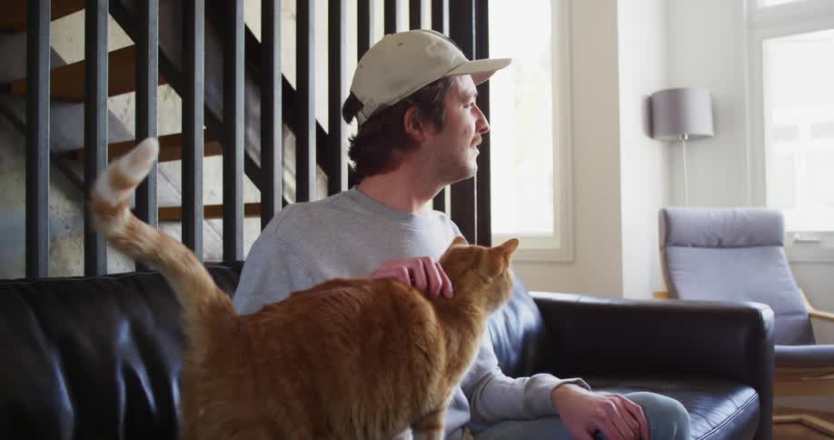 A man sitting on his couch at home petting his cat