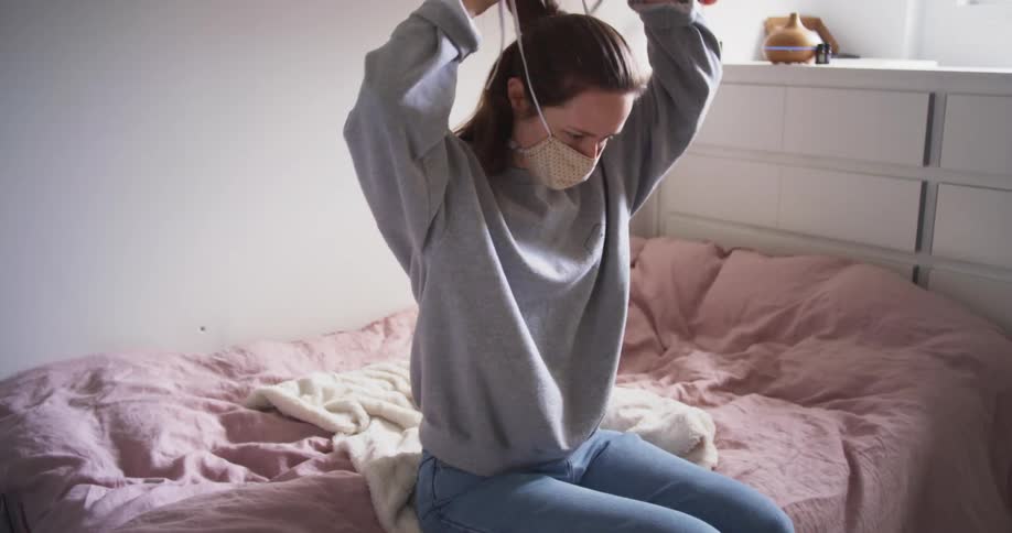 Woman sits on bed putting on face mask