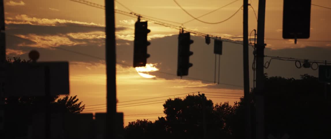 The silhouette of traffic lights poles and wires against a golden sky at sunrise