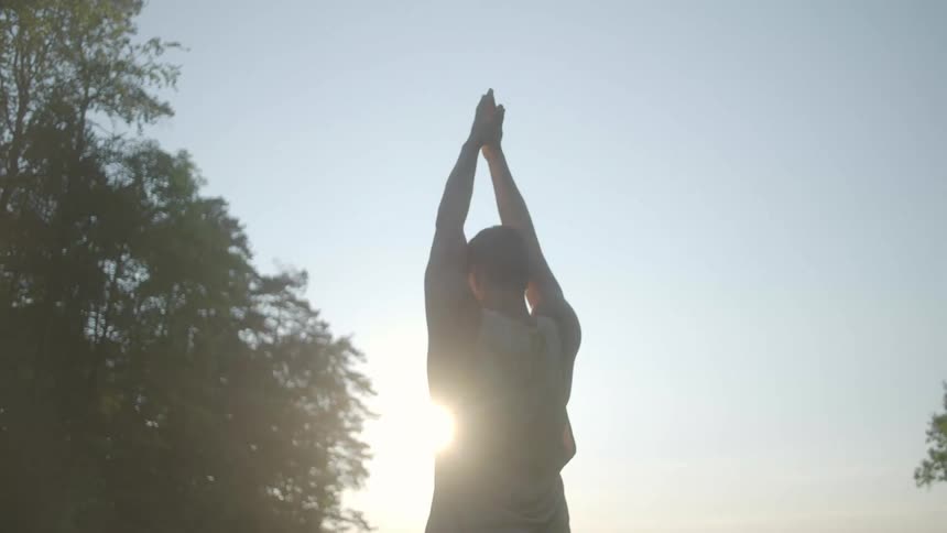 Sunlight shining onto a man standing in a field of grass doing yoga