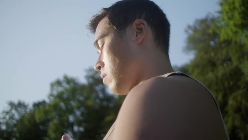 A man with his hands in front of his chest and eyes closed meditates outside on a bright sunny day
