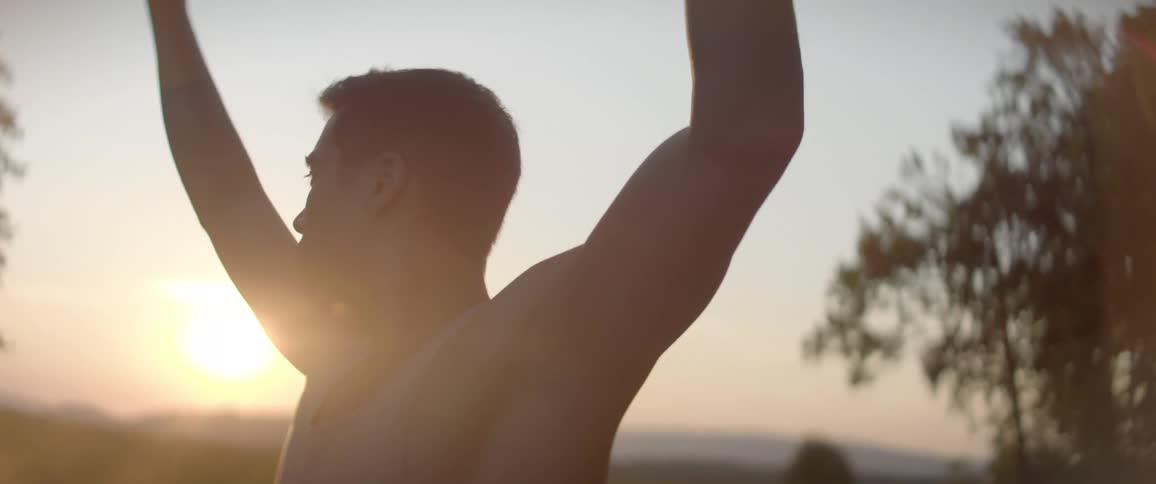 A man in a tank top does yoga in a grass field at sunset