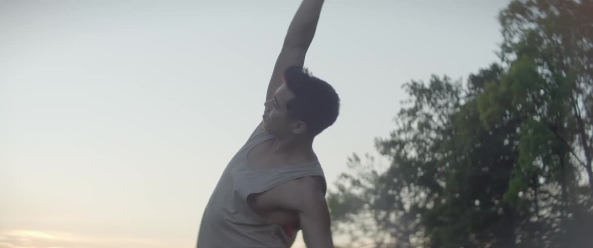 A man doing yoga stretches outdoors under the low sun