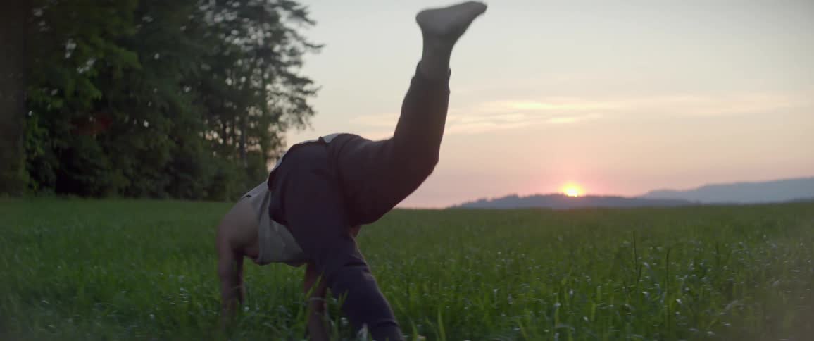 A man does a yoga hand stand outdoors in a field during the day