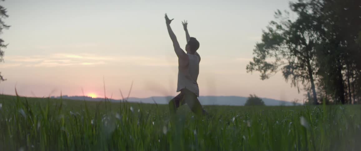 A young man practices yoga in a field