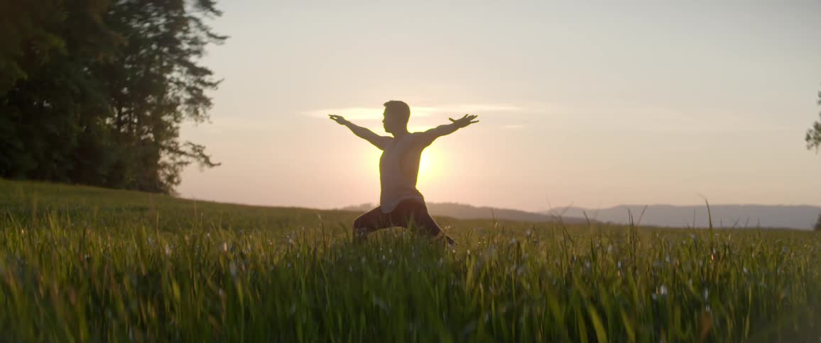 A man raises and stretches his arms out in a yoga pose at sunset