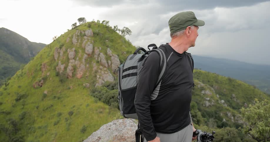 A man is standing on a mountain top holding a camera