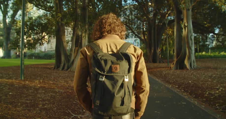 A man with a backpack and a mask walking in a pathway with buildings in the background