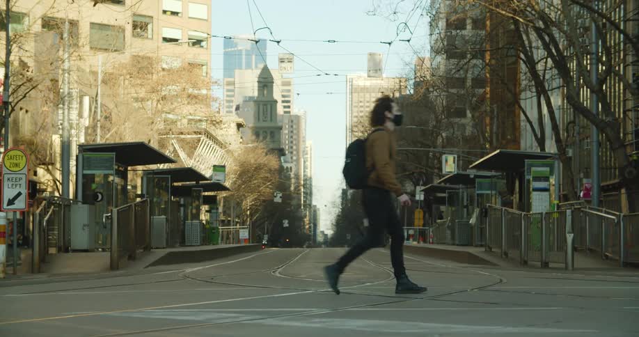 A man wearing a black medical mask cross a street in a city during the daytime