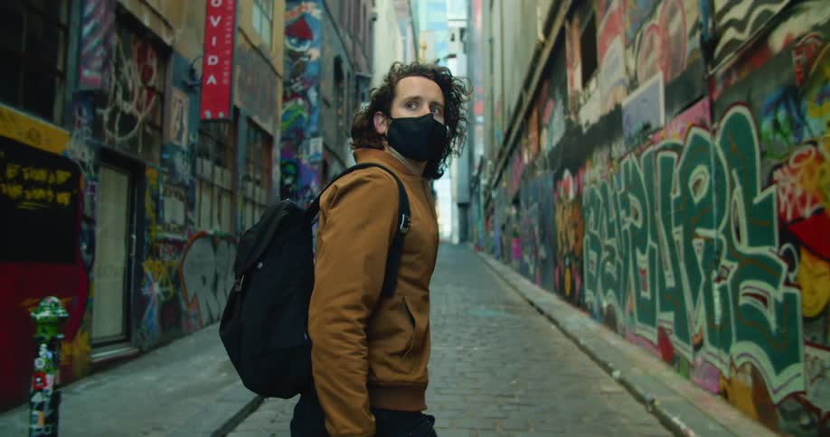 A teenager walking down a city street looks at the buildings covered in graffiti