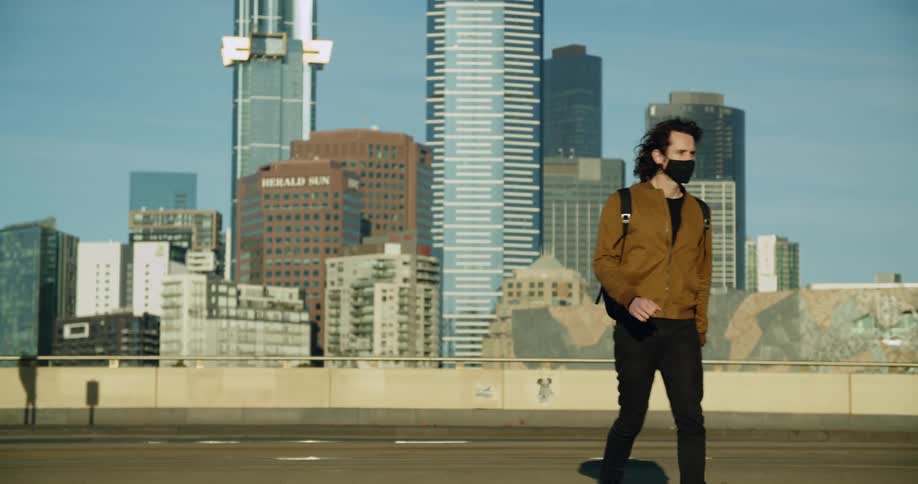 A teenager wearing a mask walking across a city street