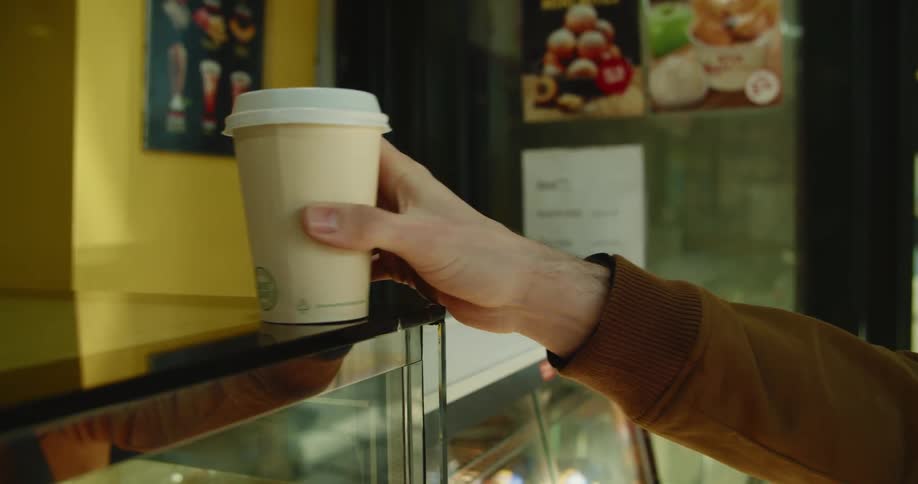 A hand picks up a coffee cup from the top of a bakery glass case