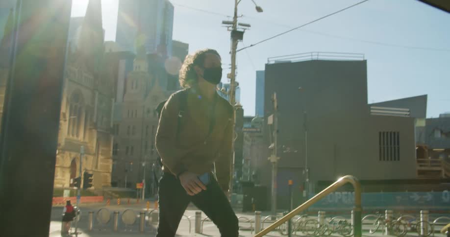 A man wearing a mask and a backpack jogs up the steps from a city plaza on a sunny day