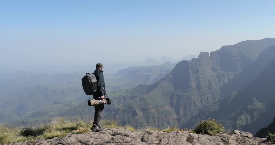 A man is hiking along a cliff holding a camera