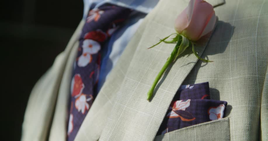 A white man with a flower pinned to his suit stands outside