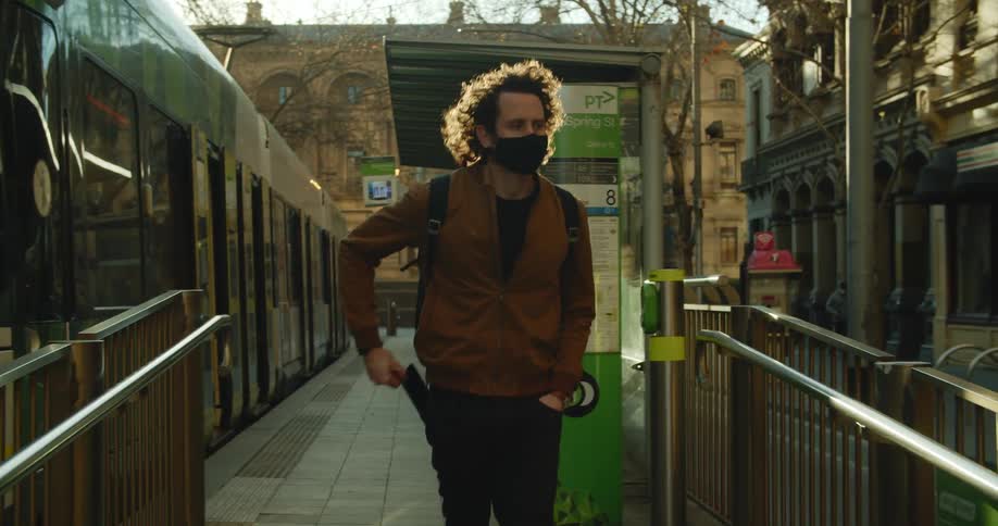 A teenager in the city walks past a bus and takes his phone out and looks at it