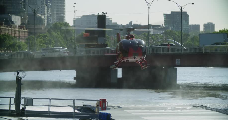 A helicopter landing on a small pier on a river in a metropolis during the day