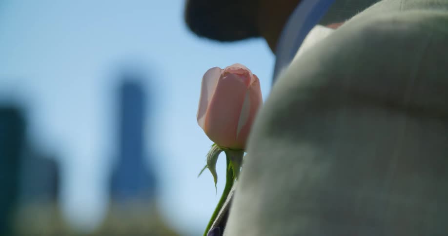 A man with a suit with a flower on it standing with buildings and skyscrapers in the background