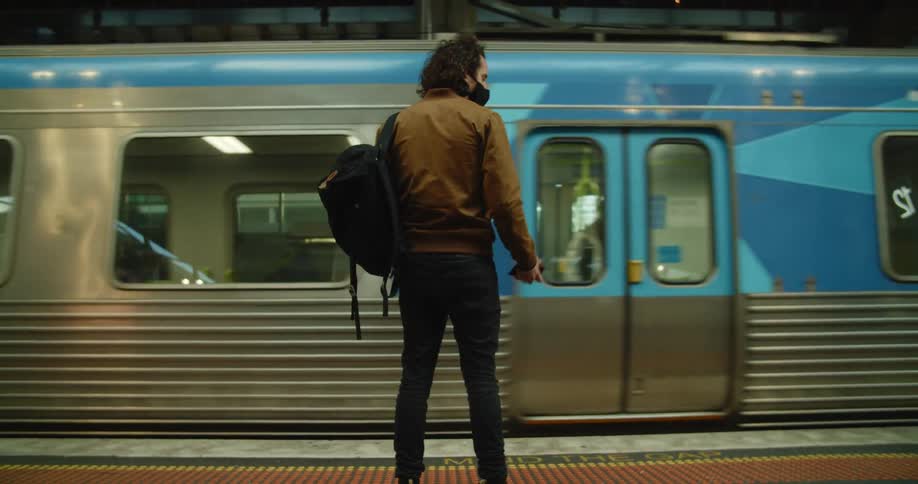 A man stands on a train platform and looks at his smart phone as a train rolls into the station