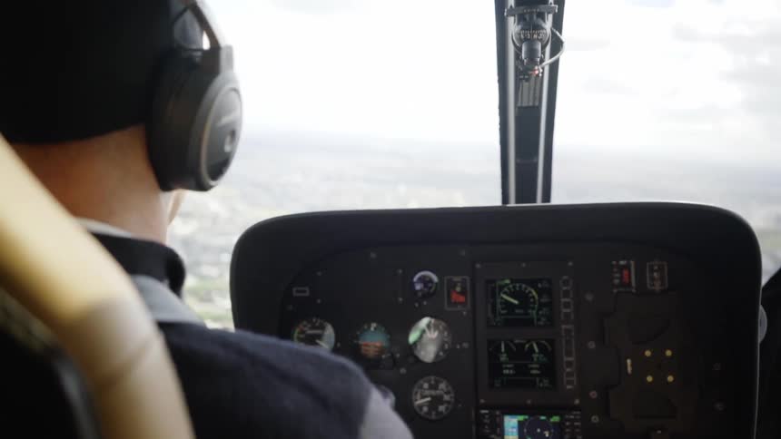 A pilot at the controls flies a helicopter on a cloudy day