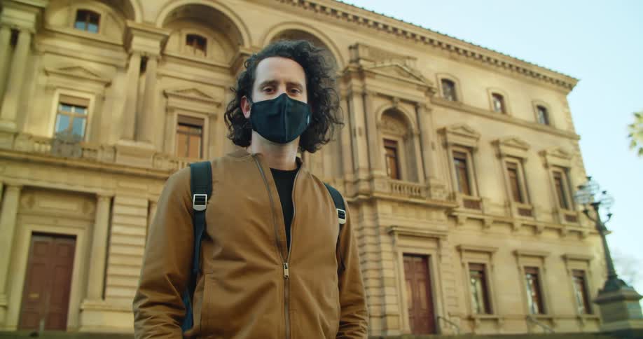 A man is standing outdoors in a city while wearing a face mask