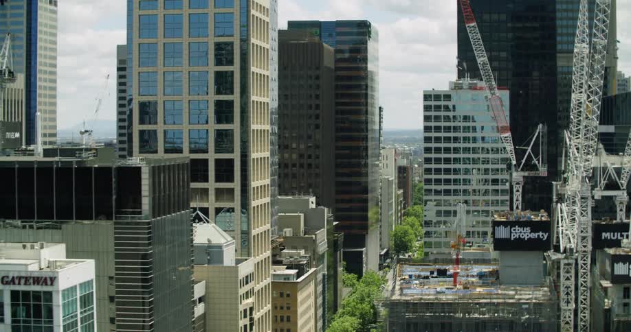 Construction cranes sit on city building rooftops as skyscraper facades reflect the sky and surrounding buildings