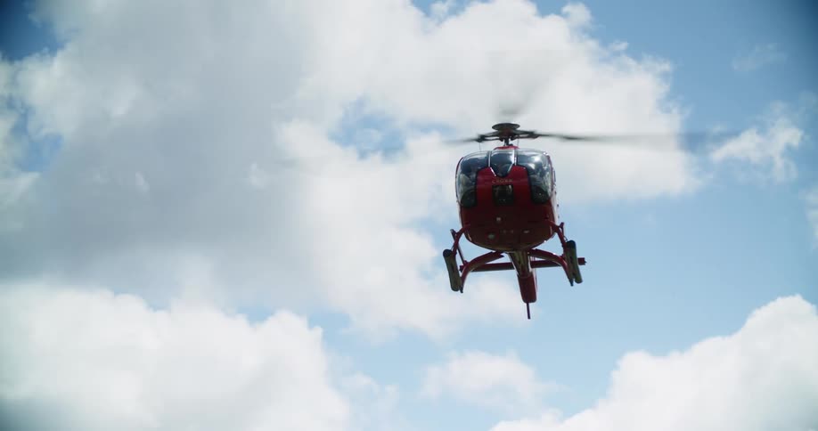 A flying helicopter lowers while flying in a bright blue sky with white clouds
