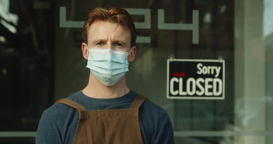 A man is standing outside of a store while wearing a mask