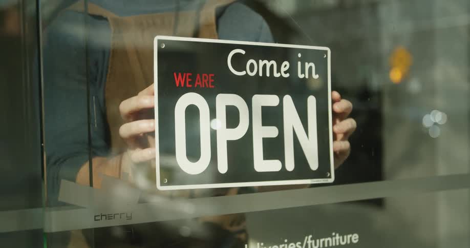 A man opens the store by turning the open sign around