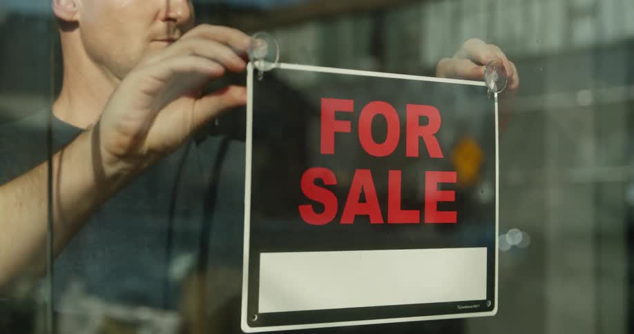 A man hangs a for sale sign on the glass front window of a business