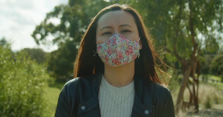 A young asian woman wears a floral mask as she stands in a park