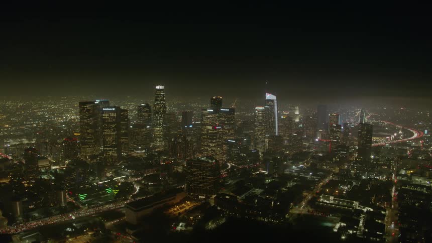 A towering metropolitan skyline is filled with numerous tall skyscrapers that are brightly illuminated at nighttime