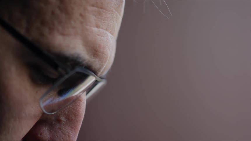 A man wearing glasses focuses intently on the task he is working on