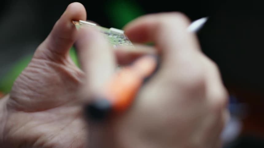 A person examining a palm sized printed circuit board in their hand