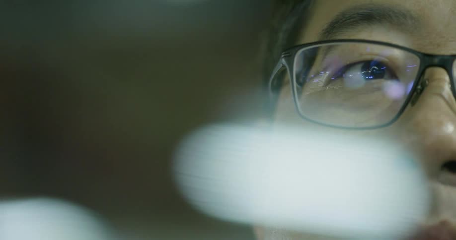 Lights reflect on the glasses of a man looking out a window