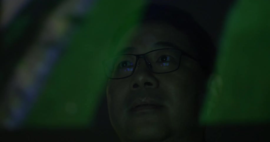 A man in glasses is visible behind a video overlay that scrolls by