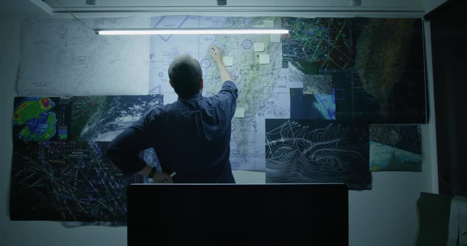 A man writes on a map hanging on a wall