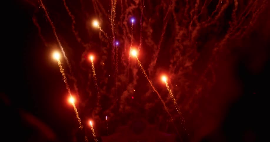 Fireworks shooting into the night sky over a building as a crowd watches