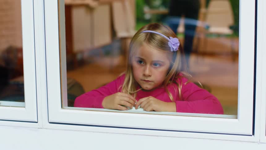 A little girls sits inside looking longingly out of a window