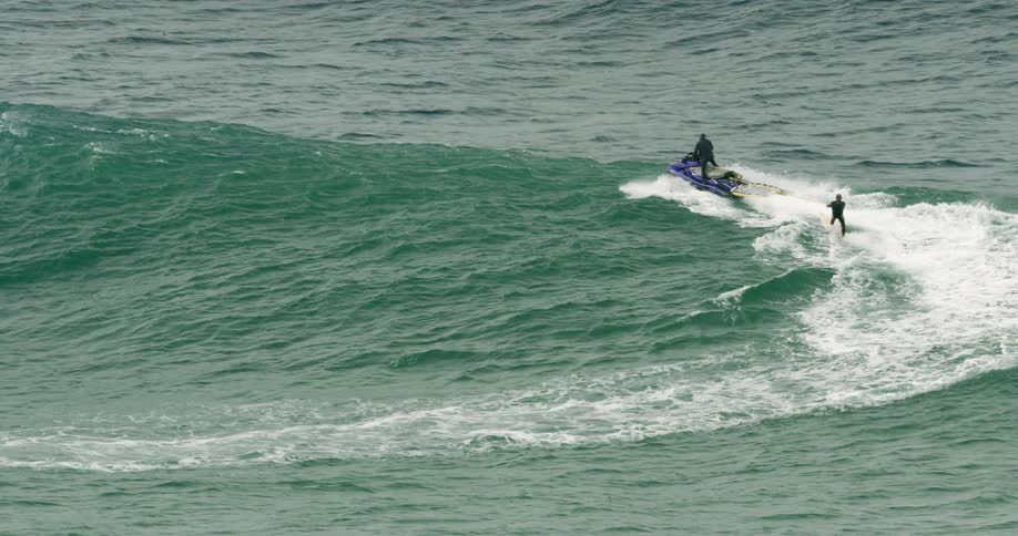 A man is surfing while being pulled by a jet ski
