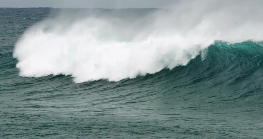 An ocean wave curls and breaks splashing and creating white foam