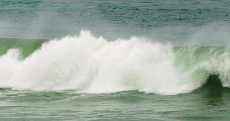 A man swims behind the tall wave on his surfboard